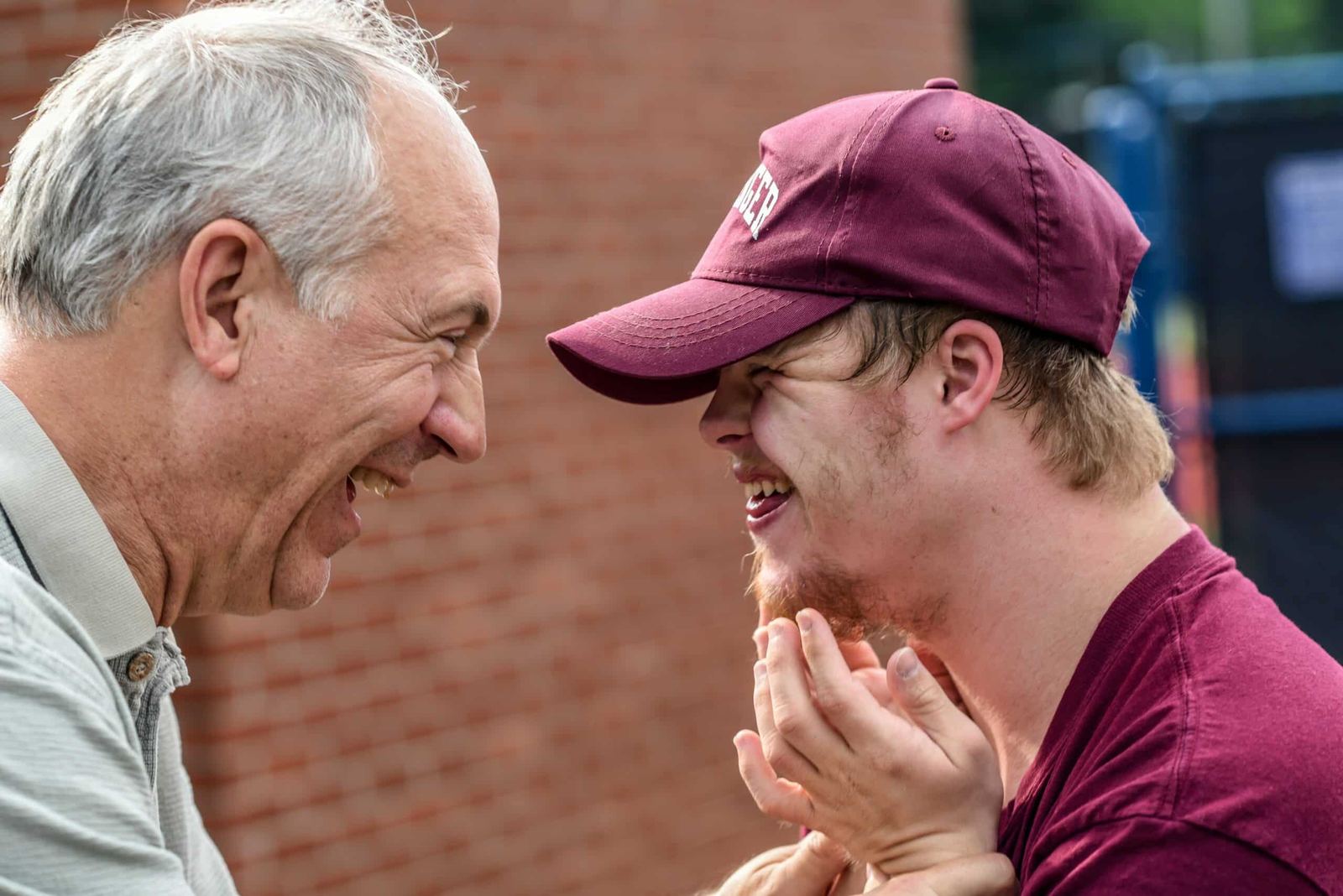 An older man and a young man with Down syndrome laughing together outdoors.