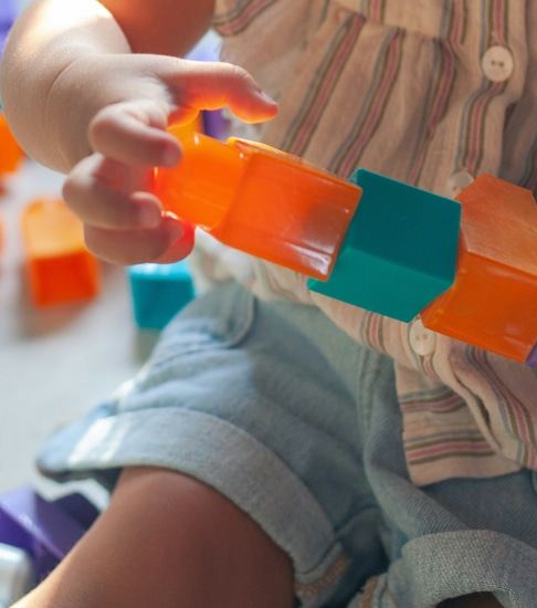 A toddler's hands stacking bright orange and teal building blocks.