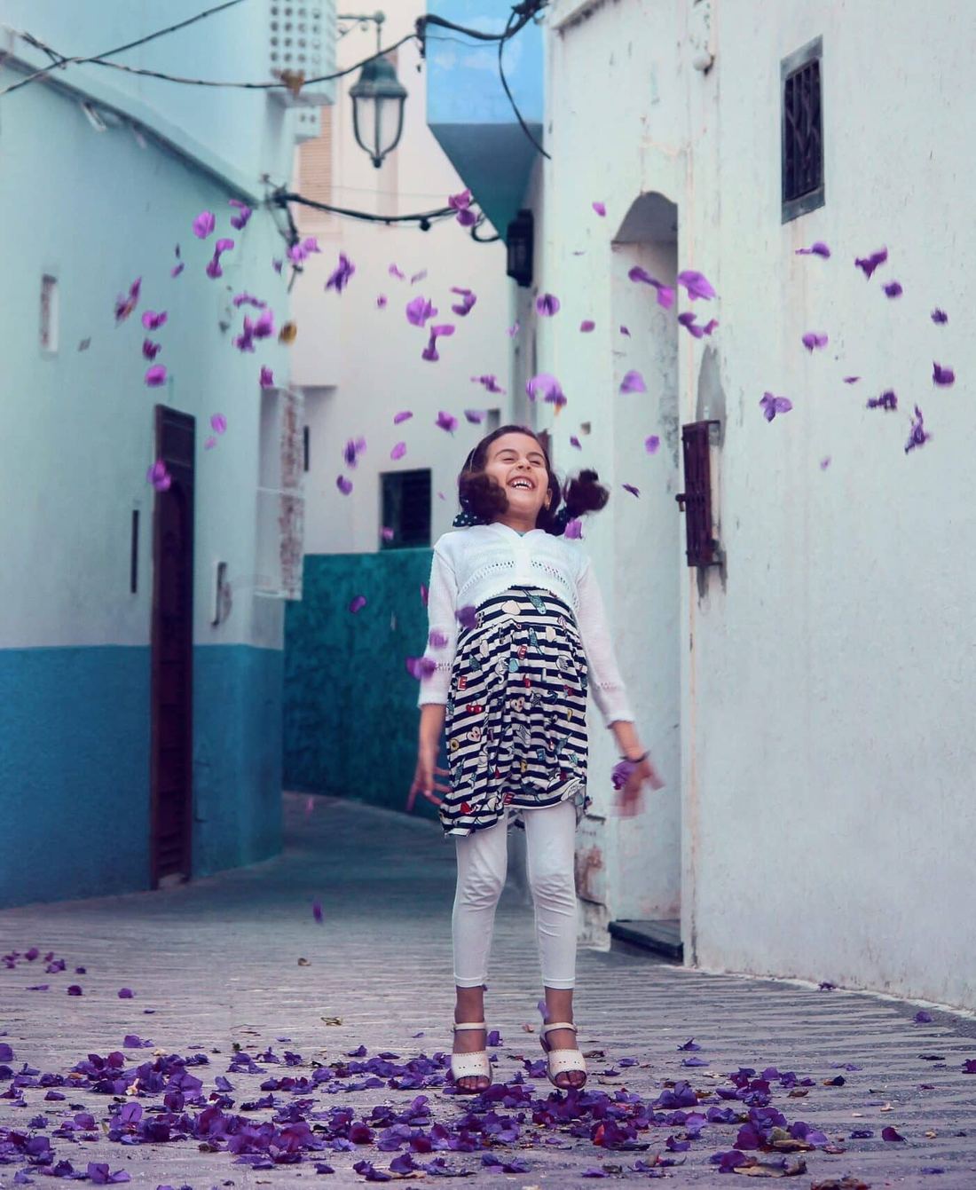 A laughing child tossing purple flower petals into the air.